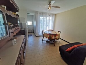 Ein Wohnzimmer mit Essbereich, Deckenventilator und sichtbarer Küche im Hintergrund.