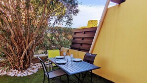 An outdoor patio with a table set for two, surrounded by chairs, a small tree, and a yellow wall. - Studio with parking, quiet and near beach - 4 guests (Cap d'Agde)