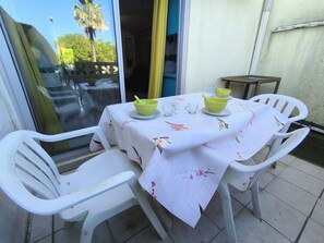 Eine Terrasse mit einem Tisch für zwei Personen, weißen Plastikstühlen und einer Glastür, die zu einem Garten führt.