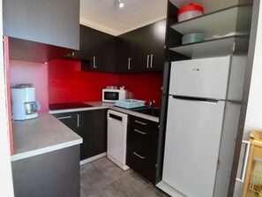 A compact kitchen with black cabinets, a white refrigerator, a microwave, and a coffee maker. - 3-room apartment - 6 guests, Cap d'Agde (Cap d'Agde)