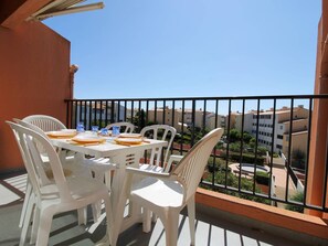 A balcony with a table set for four, white plastic chairs, and a view of buildings in the background. - 3-room apartment - 6 guests, Cap d'Agde (Cap d'Agde)