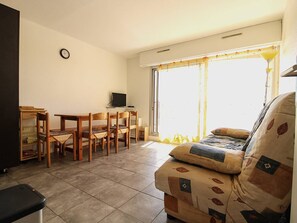 A living room with a sofa, a TV, a dining table with chairs, and a window with curtains. - 3-room apartment - 6 guests, Cap d'Agde (Cap d'Agde)