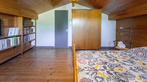Una habitación con pisos de madera, una cama con ropa de cama estampada, una estantería, un armario y una silla colgante.