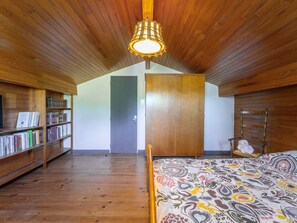 Ein Zimmer mit Holzboden, einem Bett mit gemusterten Betttextilien, einem Bücherregal, einem Kleiderschrank und einem Hängekorbsessel.