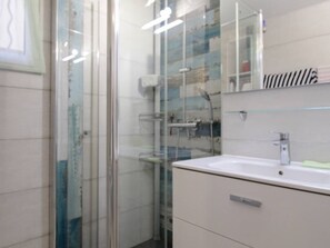 Ein Badezimmer mit Duschkabine aus Glas, einem weißen Waschbecken und einem Spiegel darüber.