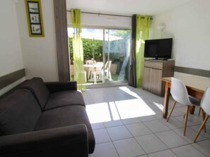 Ein Wohnbereich mit einer Couch, einem Fernseher, einem Esstisch mit Stühlen und einer Glastür zum Außenbereich.