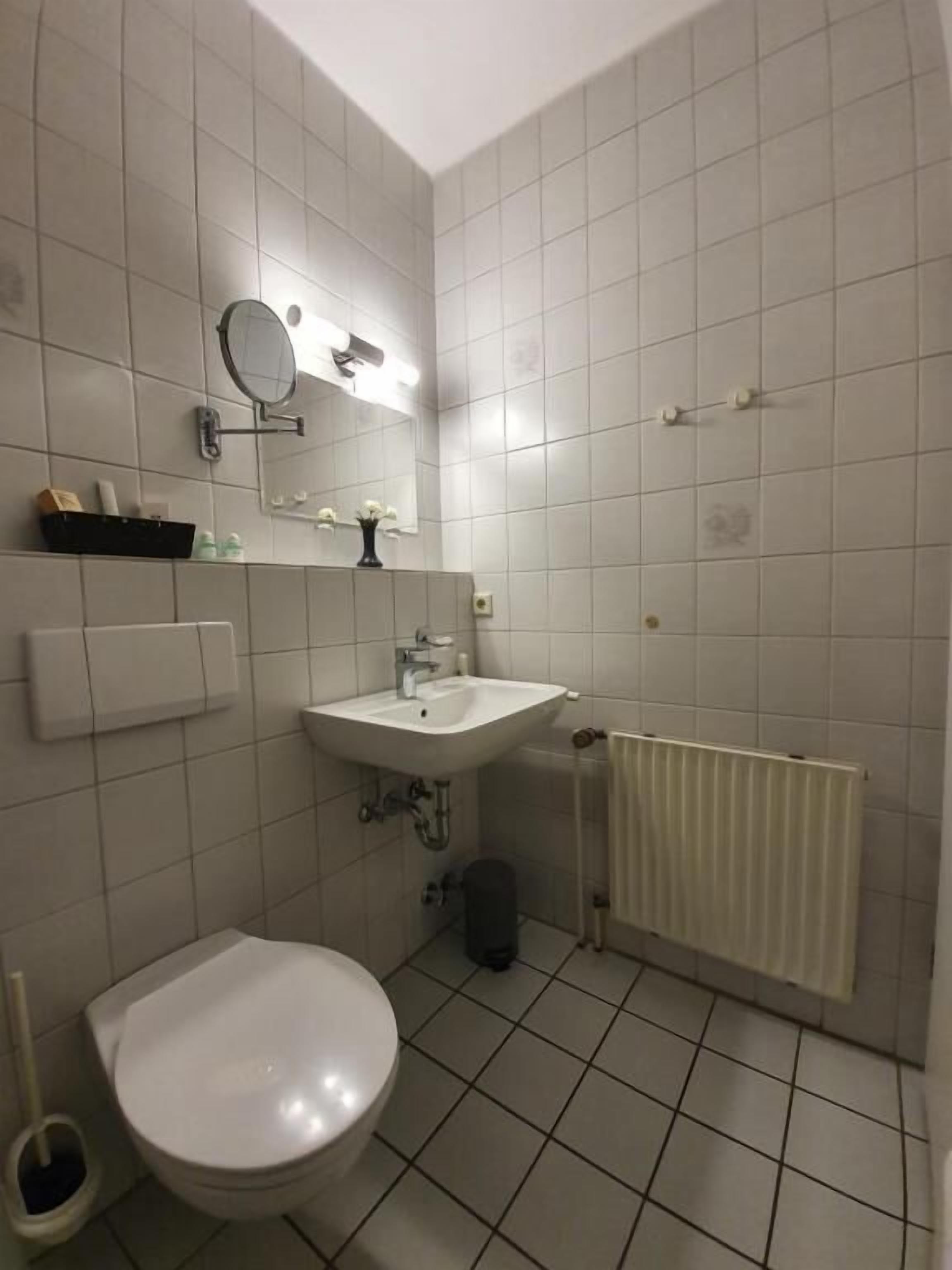 A bathroom with a toilet, sink, mirror, and tiled walls.