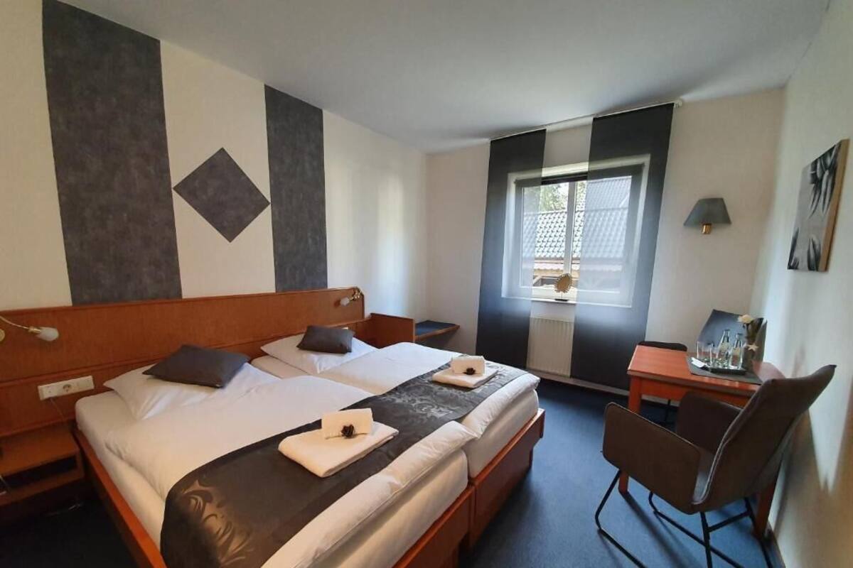A hotel room with a large bed, a desk, a chair, and a window with blinds.