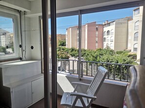 Ein Balkon mit weißem Stuhl, einem Fenster und Blick auf Häuser und Grünflächen.