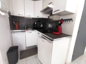 Eine kleine Küche mit weißen Schränken, einem Geschirrspüler, einer Mikrowelle und einer roten Kaffeemaschine.