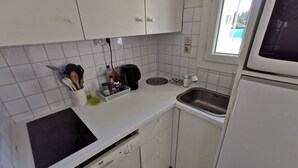 Una cocina compacta con armarios blancos, lavavajillas, un lavabo y una ventana.