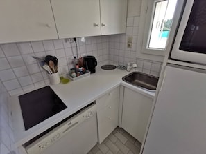 A compact kitchen with white cabinets, a dishwasher, a sink, and a window. - Apartment with AC, pool, near beaches - 8 guests (Cap d'Agde)