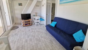 Una habitación con sofá, televisión, una mesita y una silla.
