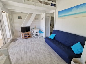 A room with a sofa, a TV, a small table, and a chair. - Apartment with AC, pool, near beaches - 8 guests (Cap d'Agde)