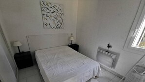 Un dormitorio con una cama, dos mesitas de noche, un radiador y una ventana.