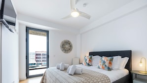 Ein Schlafzimmer mit Bett, Deckenventilator, Nachttisch mit Lampe und Blick ins Freie.
