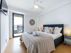 Ein Schlafzimmer mit Bett, Deckenventilator, Nachttisch mit Lampe und Blick ins Freie.