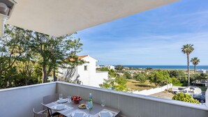 A balcony with a table set for two, overlooking a coastal view with palm trees and buildings. - Lagos Line Apartment - sea views and Meia Praia (Lagos)