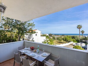 Ein Balkon mit Tisch für zwei Personen, mit Blick auf die Küste, Palmen und Gebäude.