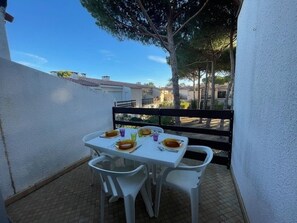 Eine kleine Terrasse im Freien mit einem für zwei Personen gedeckten Tisch, umgeben von weißen Plastikstühlen.