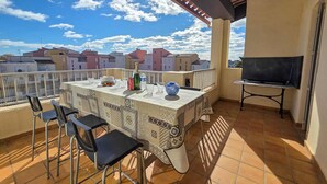 Une terrasse avec une table dressée pour deux personnes, un téléviseur et une vue sur les bâtiments.