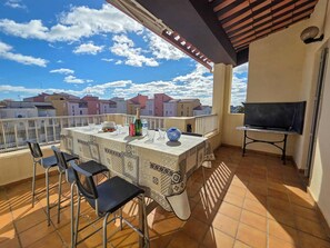 Eine Terrasse mit Tisch für zwei Personen, einem Fernseher und Blick auf Gebäude.