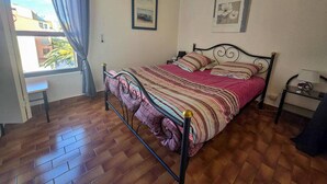 Une chambre à coucher avec un lit, une fenêtre avec des rideaux, une table de chevet et un mur orné de deux tableaux encadrés.