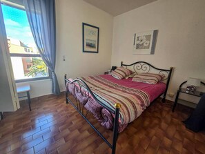 Ein Schlafzimmer mit einem Bett, einem Fenster mit Vorhängen, einem Nachttisch und einer Wand mit zwei gerahmten Bildern.