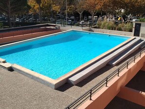 A rectangular swimming pool with a clear blue water surface, surrounded by a low stone wall and a metal railing. - Cozy studio near the beach - 3 guests (Cap d'Agde)