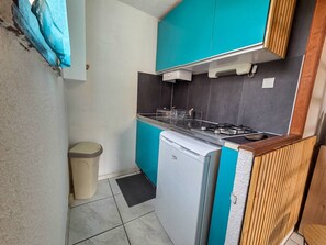 Eine kleine Küche mit türkis-blauen Schränken, einem weißen Kühlschrank und einem Gasherd.
