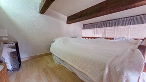 Ein Schlafzimmer mit einem hölzernen Bett, einem Fenster mit transparenten Vorhängen und einem Holzboden.