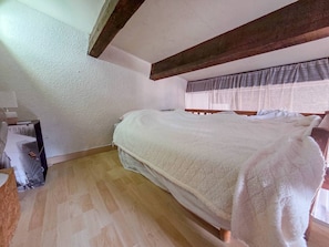 Ein Schlafzimmer mit einem hölzernen Bett, einem Fenster mit transparenten Vorhängen und einem Holzboden.
