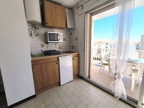 Eine kompakte Küche mit Mikrowelle, kleinem Kühlschrank und Spüle. Eine Glastür führt zu einem Außenbereich mit Blick auf Gebäude.