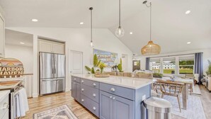 A modern kitchen with a large island, stainless steel appliances, pendant lighting, and a view to the outdoors. - Harbor Haven | Hot Tub | Pool Access | Gym | Sauna (South Haven)