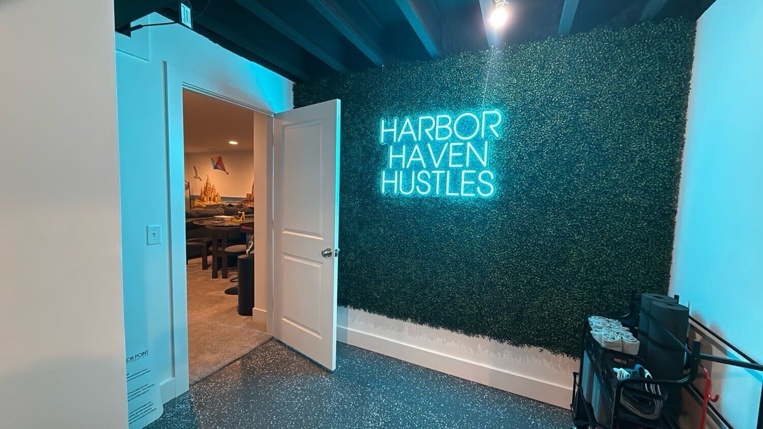 A hallway with a neon sign reading 'HARBOR HAVEN HUSTLES' on a textured wall.