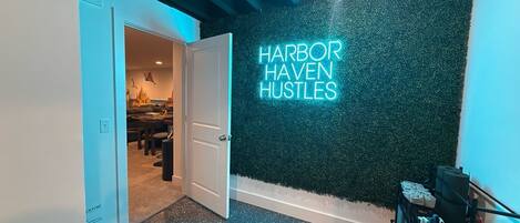 A hallway with a neon sign reading 'HARBOR HAVEN HUSTLES' on a textured wall.
