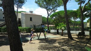 Ein Spielplatz mit Schaukeln und Rutsche, umgeben von Bäumen und einem Gebäude.