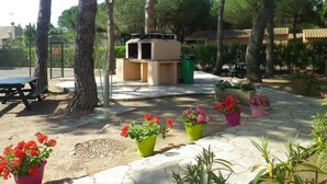 Eine Terrasse mit Grill, Picknicktisch und Topfpflanzen.