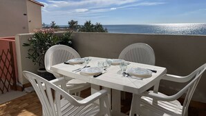 Une table blanche dressée pour quatre personnes, avec des chaises, une plante en pot et une vue sur la mer.
