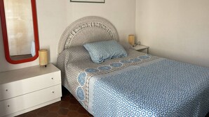 Une chambre à coucher avec un lit, une commode, une table de chevet, une lampe et un tableau encadré au mur.