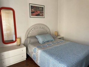 A bedroom with a bed, a dresser, a nightstand, a lamp, and a framed picture on the wall. - 2-room apartment sea view - 4 guests (Cap d'Agde)