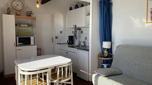 Une cuisine compacte avec un plan de travail blanc, une table à manger avec des chaises, un canapé gris et une petite table d’appoint avec une lampe.