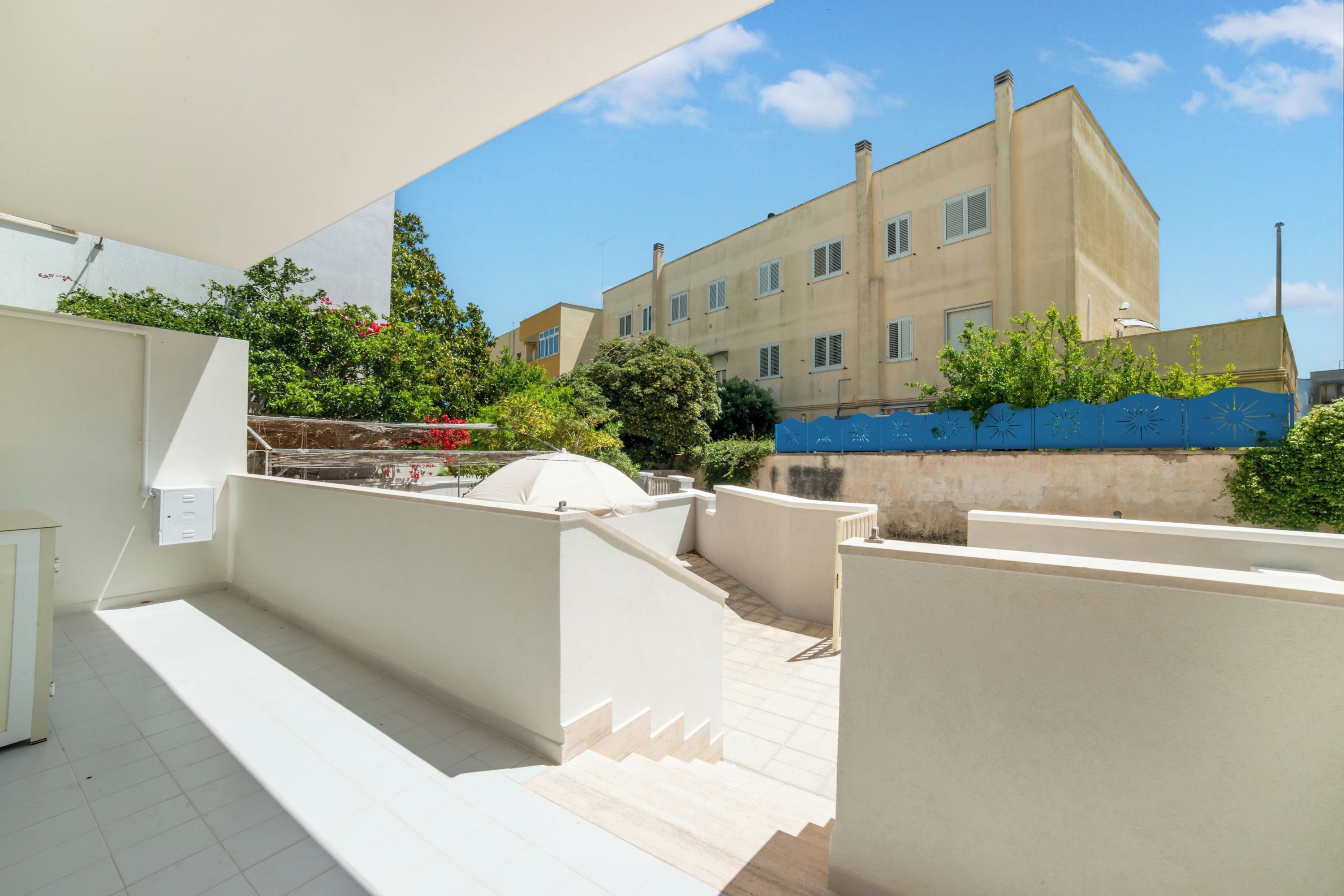 Terraço no telhado com guarda-corpo branco, um espaço de estar ao ar livre e vista para um edifício alto ao fundo.