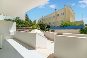 A rooftop terrace with a white railing, a small outdoor seating area, and a view of a multi-story building in the background. - Trilocale Sole in Otranto Near the Sea (Otranto)
