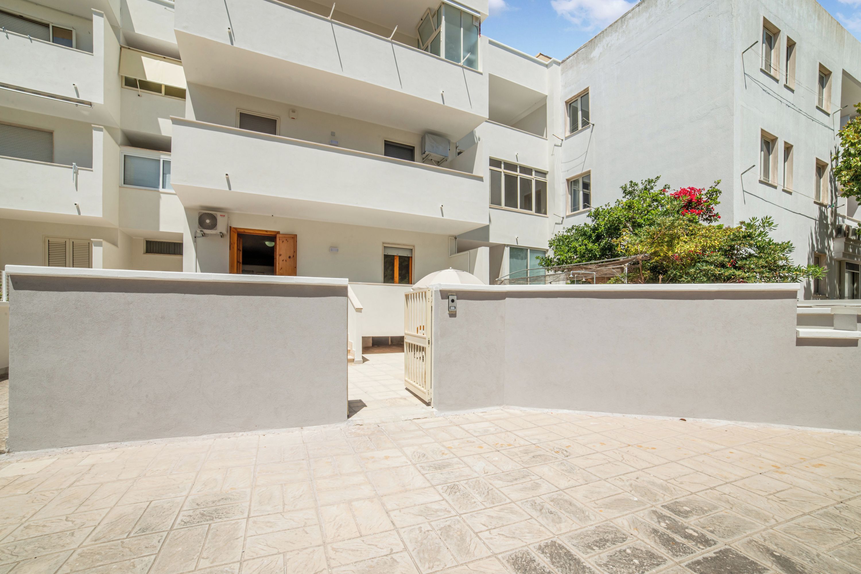 Un edificio residencial de varios pisos con balcones, una entrada porticada y un patio empedrado.