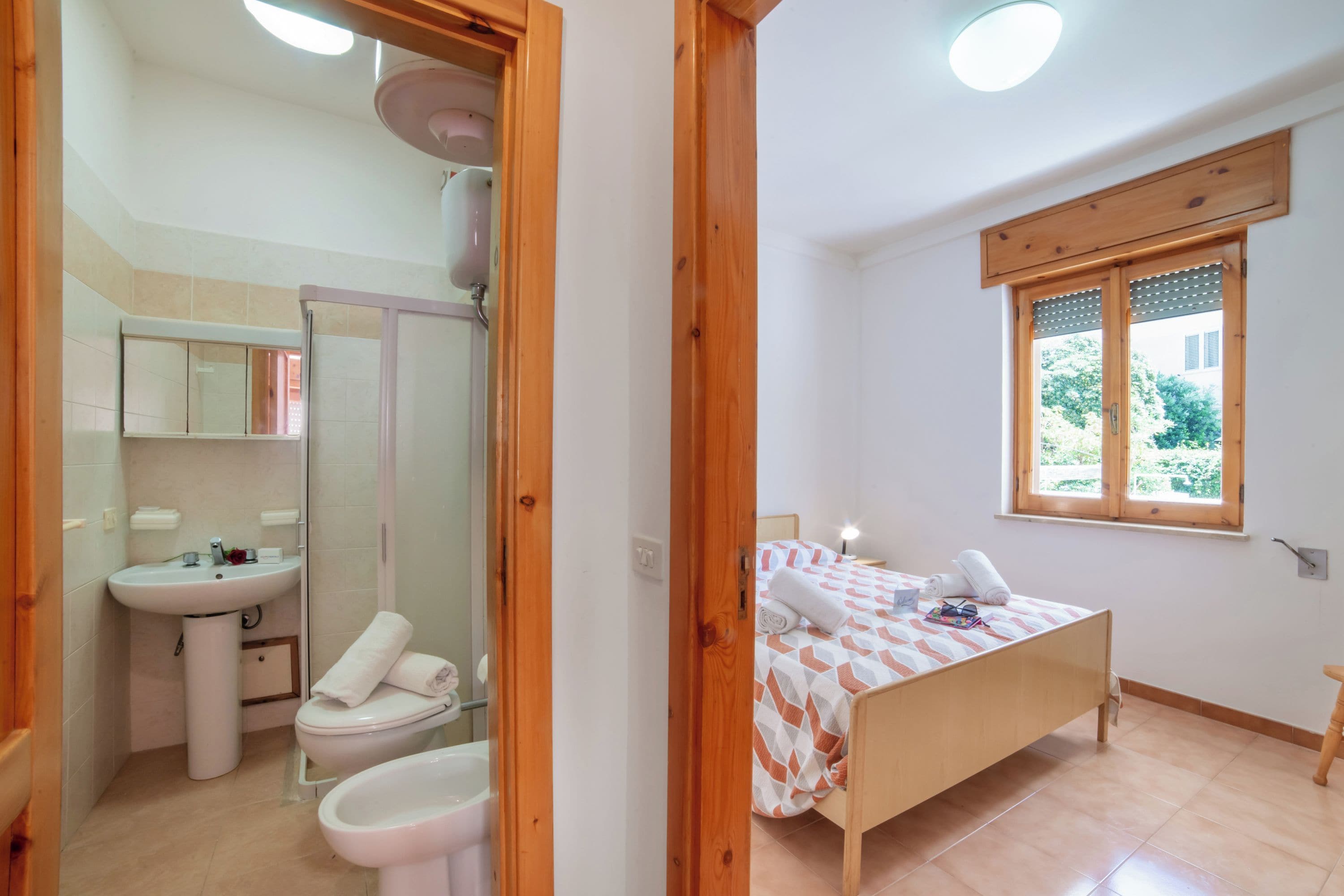 Ein Schlafzimmer mit einem Holzbett, einem Fenster mit Blick, einem Nachttisch und einem Badezimmer mit Waschbecken und Toilette.