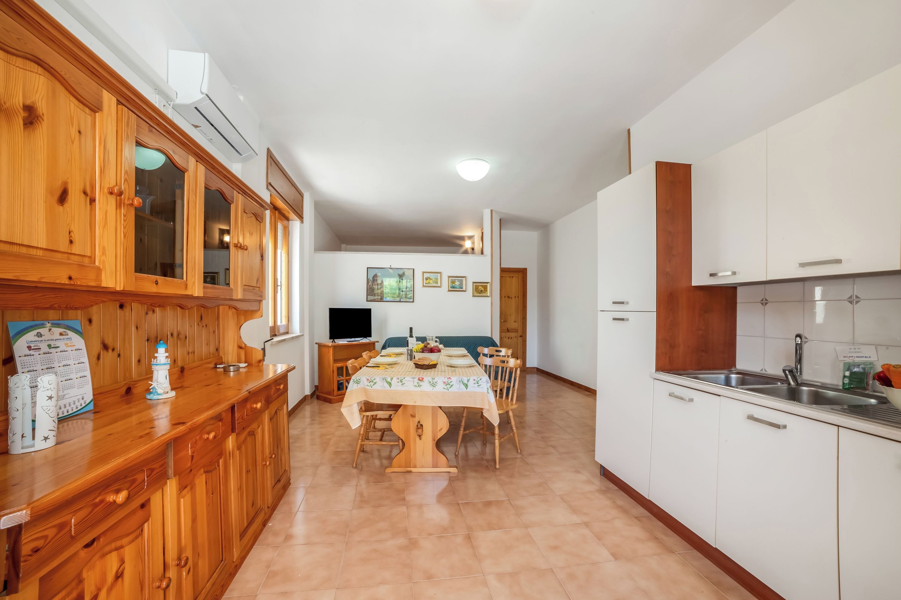 A kitchen with wooden cabinets, a dining table with chairs, a TV, and a refrigerator.