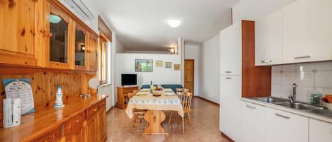 A kitchen with wooden cabinets, a dining table with chairs, a TV, and a refrigerator.