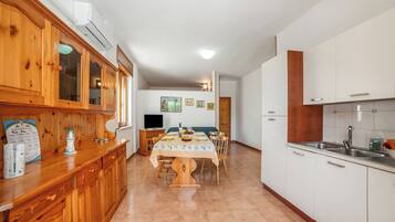 Uma cozinha com armários de madeira, uma mesa de jantar com cadeiras, uma televisão e uma geladeira.