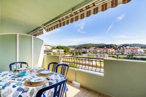 Ein Balkon mit Esstisch, der auf eine Stadtlandschaft mit Gebäuden und Hügeln blickt.